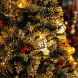 Close-up of Christmas tree branches showing illuminated mini white house, golden bauble, pine cones, and red berries among warm white LEDs