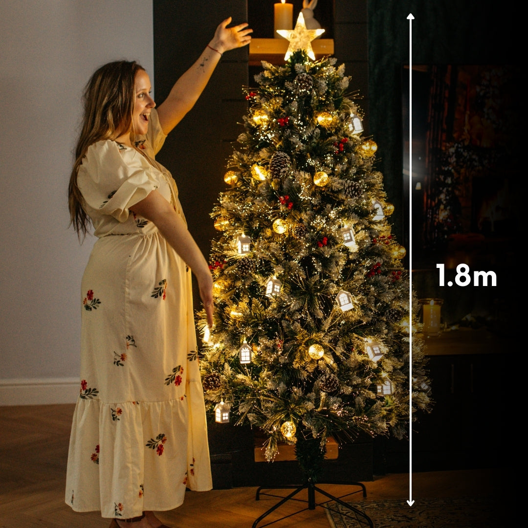 Woman reaching toward the star topper of a 1.8m prelit Christmas tree with height measurement marker showing 1.8 metres