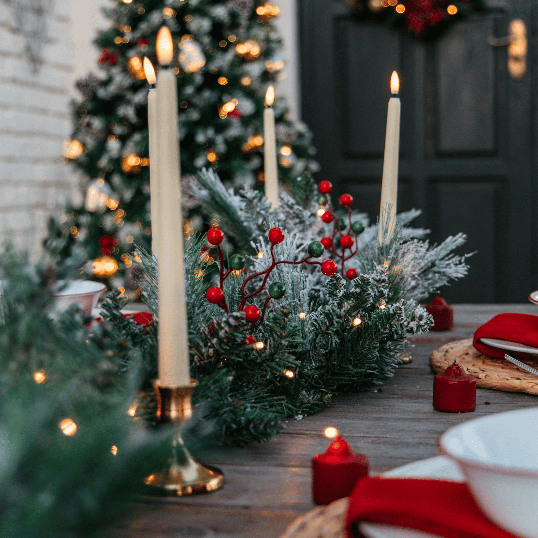 Snow-flocked garland on an outdoor Christmas table setting with a lit tree and taper candles