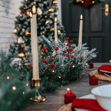 Snow-flocked garland on an outdoor Christmas table setting with a lit tree and taper candles