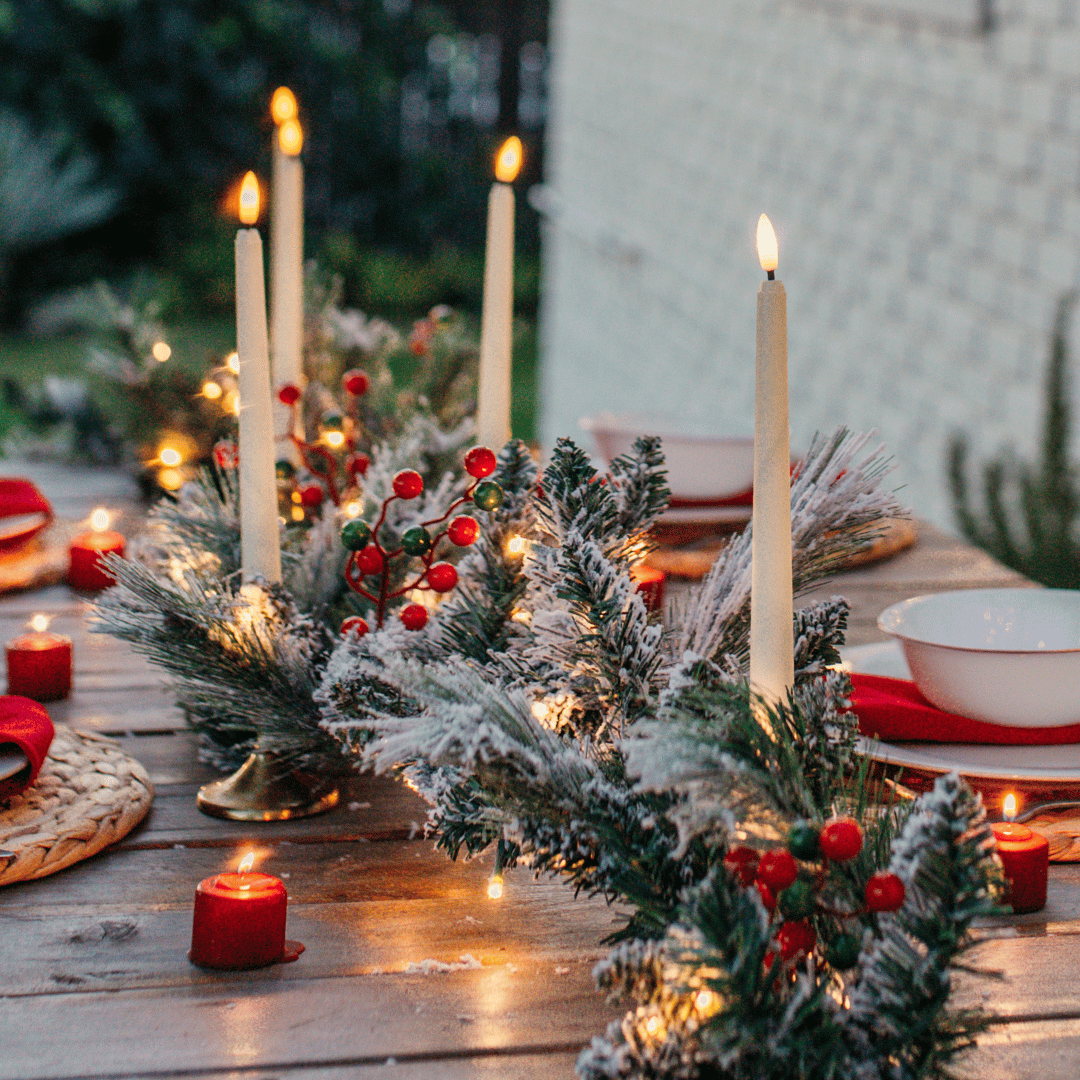 Snow-flocked pine garland with red and green berries styled as a Christmas table centrepiece with taper candles
