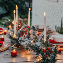 Snow-flocked pine garland with red and green berries styled as a Christmas table centrepiece with taper candles
