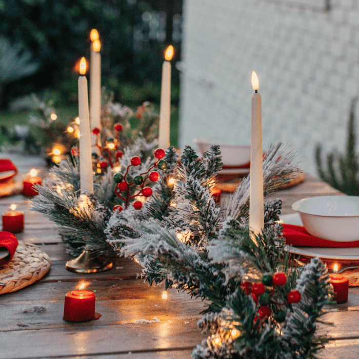 Snow-flocked pine garland with red and green berries styled as a Christmas table centrepiece with taper candles