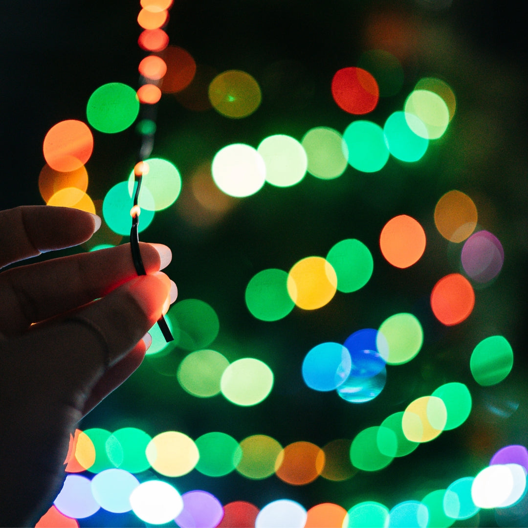 Hand holding milti-coloured fairy lights in front of colourful blurred lights
