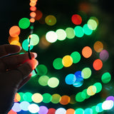 Hand holding milti-coloured fairy lights in front of colourful blurred lights