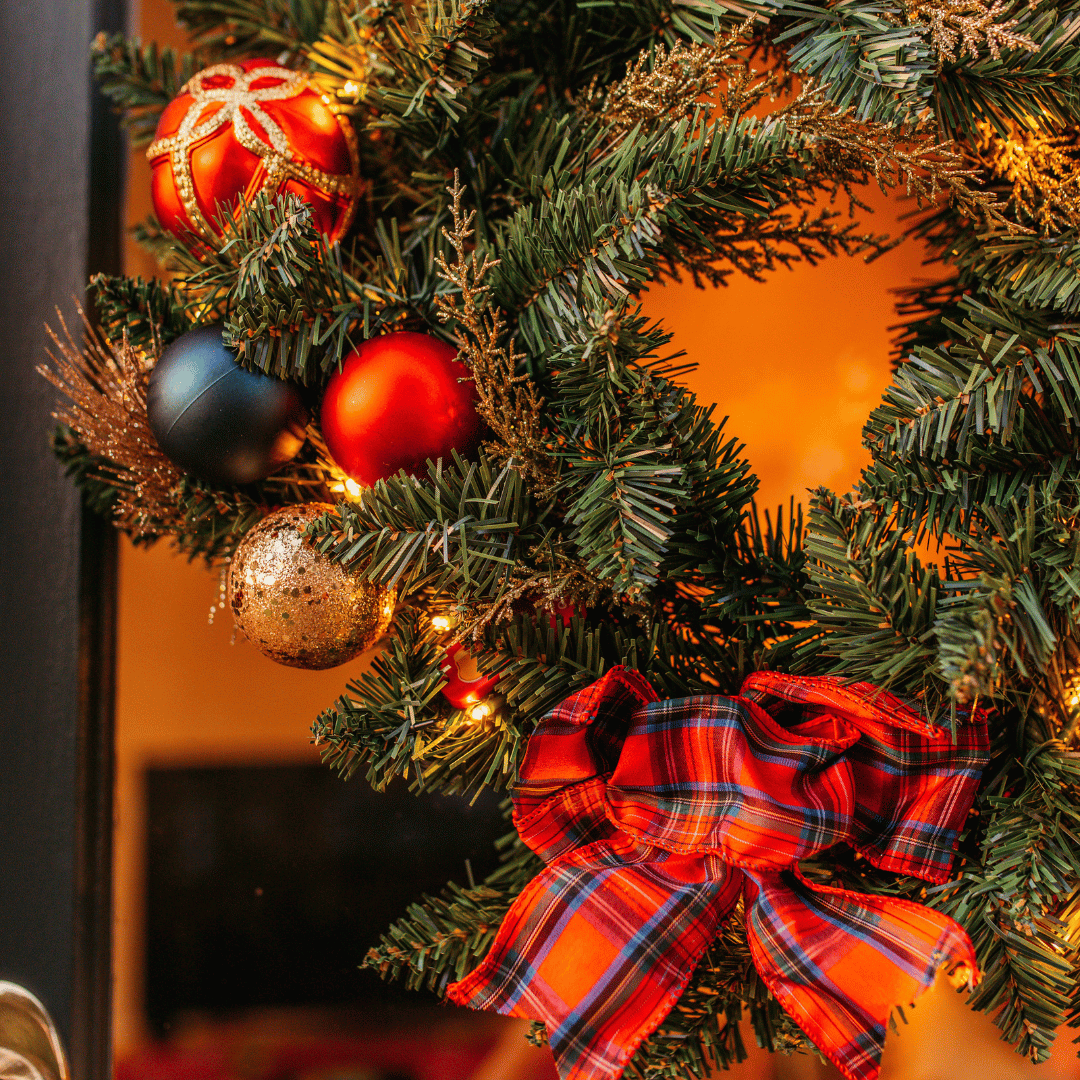 Close-up of Christmas wreath showing red, navy and gold ornaments beside a red tartan bow
