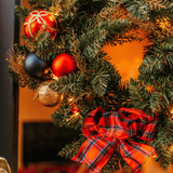 Close-up of Christmas wreath showing red, navy and gold ornaments beside a red tartan bow