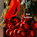 Close-up of red baubles on a luxury Christmas wreath beside a red velvet bow