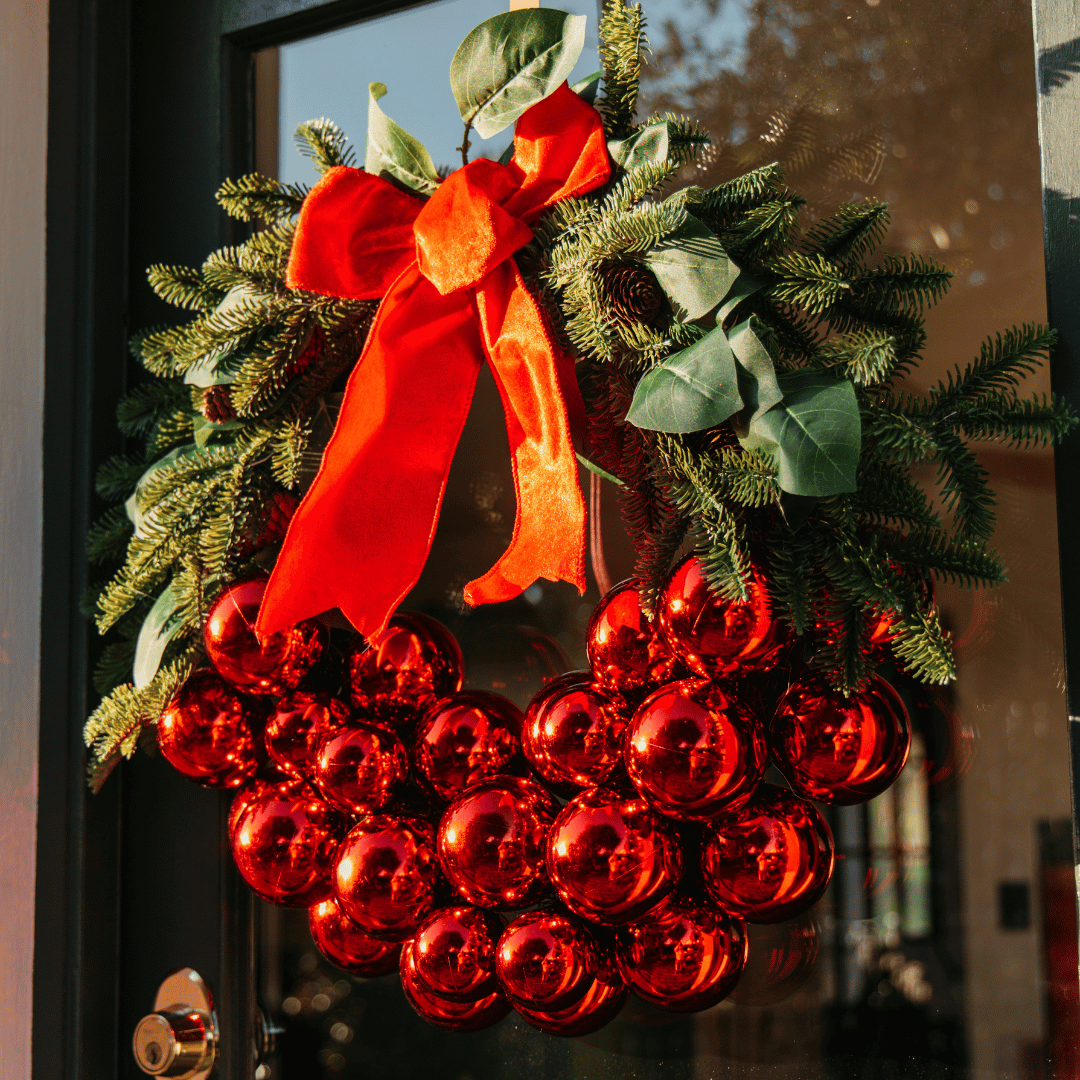 Luxury Christmas wreath with red bauble cluster hanging on a glass door in warm evening light