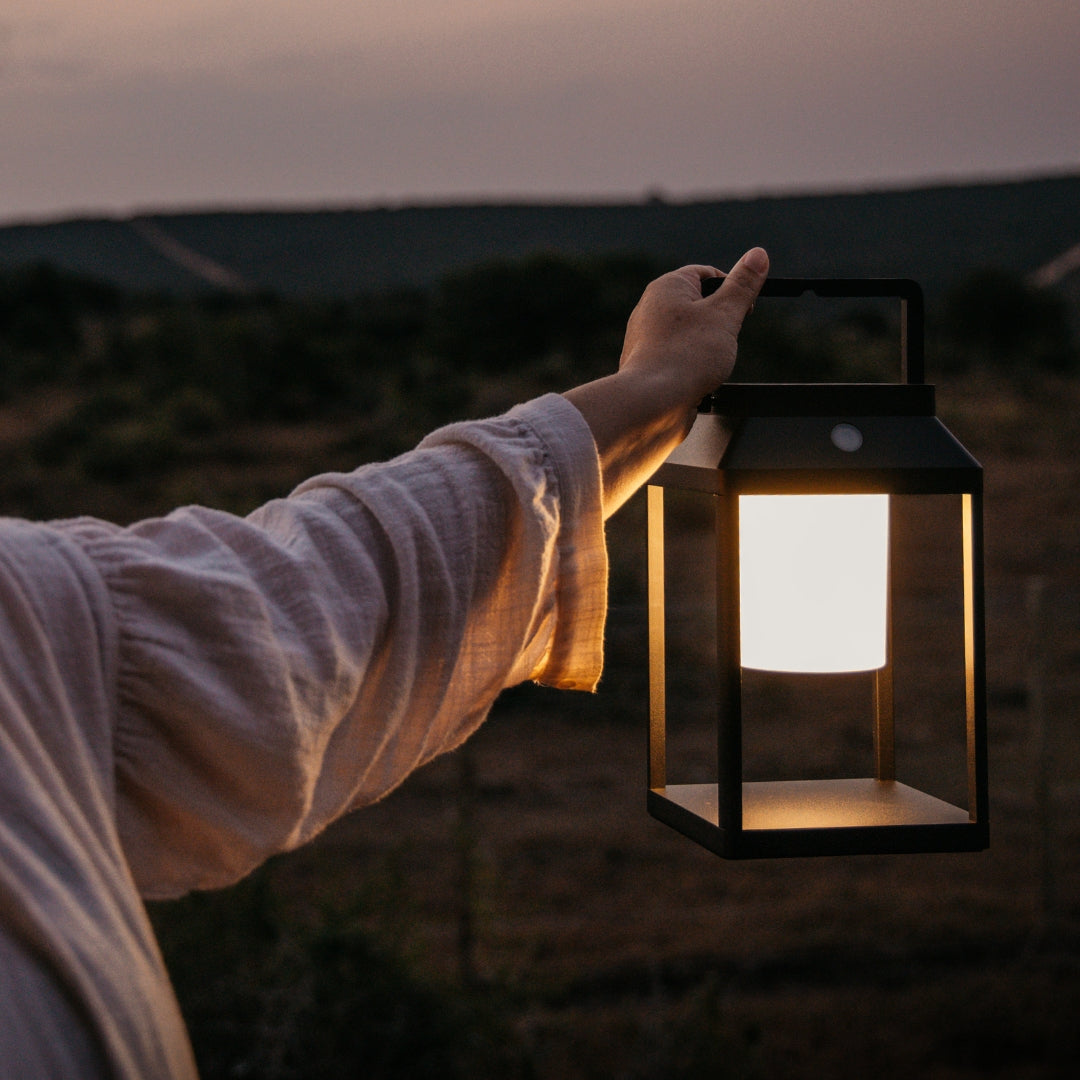 Person holding a lit Solar Glow lantern against a dark landscape