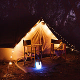 Bluetooth Speaker Lantern glowing warm white in a camping or glamping outdoor setting providing music and mood lighting