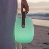 Person holding a glowing green portable light with a wooden handle on a beach.