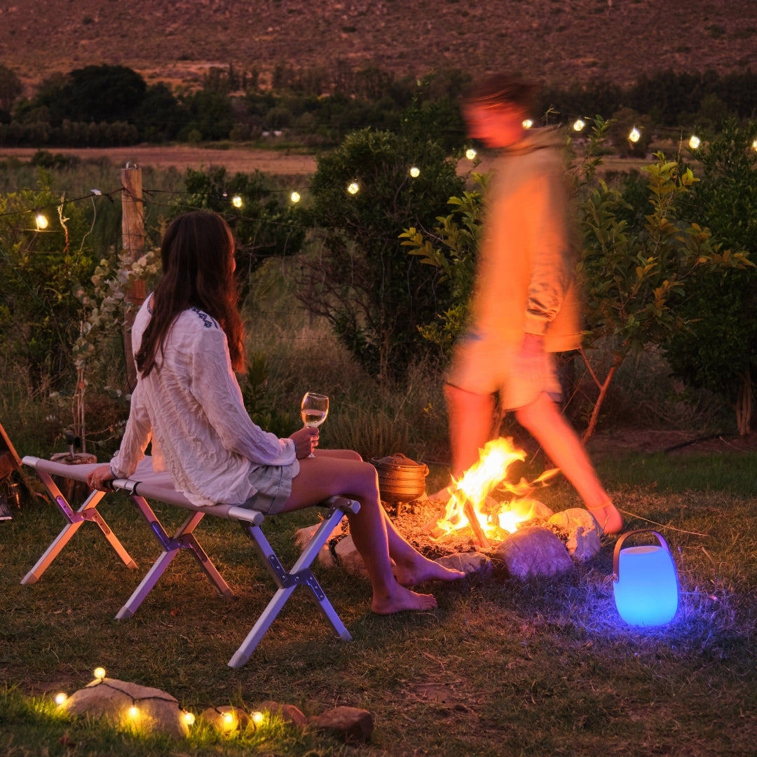 Bluetooth Speaker Lantern glowing warm white on an outdoor patio or braai table at dusk with warm ambient atmosphere