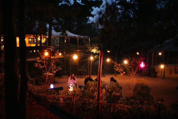 People sitting outdoors at night with string lights and a tent in the background