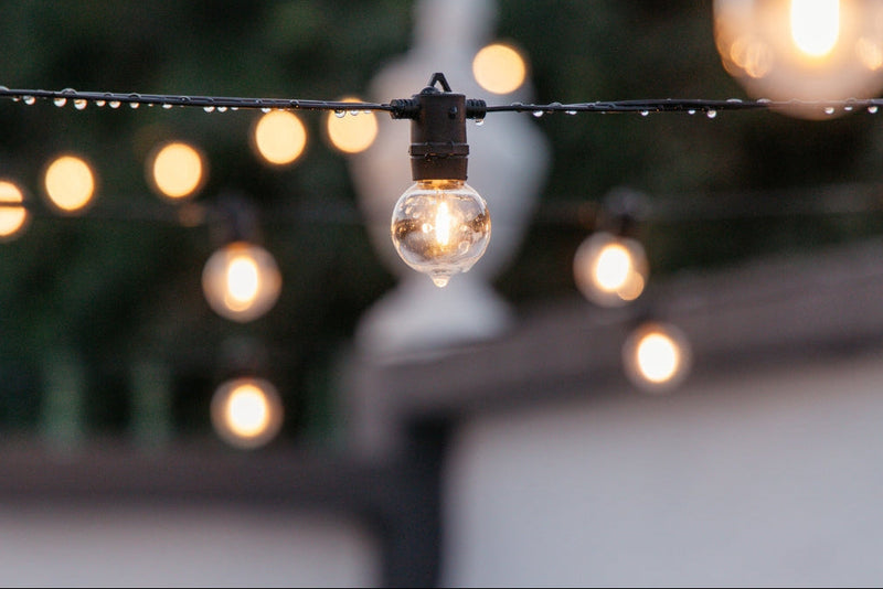 Classic String Lights Pro strung overhead with droplets after rain has come through, still glowing.