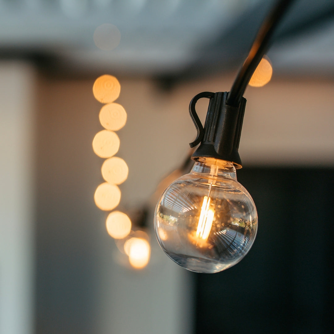 Classic String Lights with 25 warm white G40 globe bulbs on black cable glowing in a styled South African outdoor space creating a warm golden atmosphere at dusk