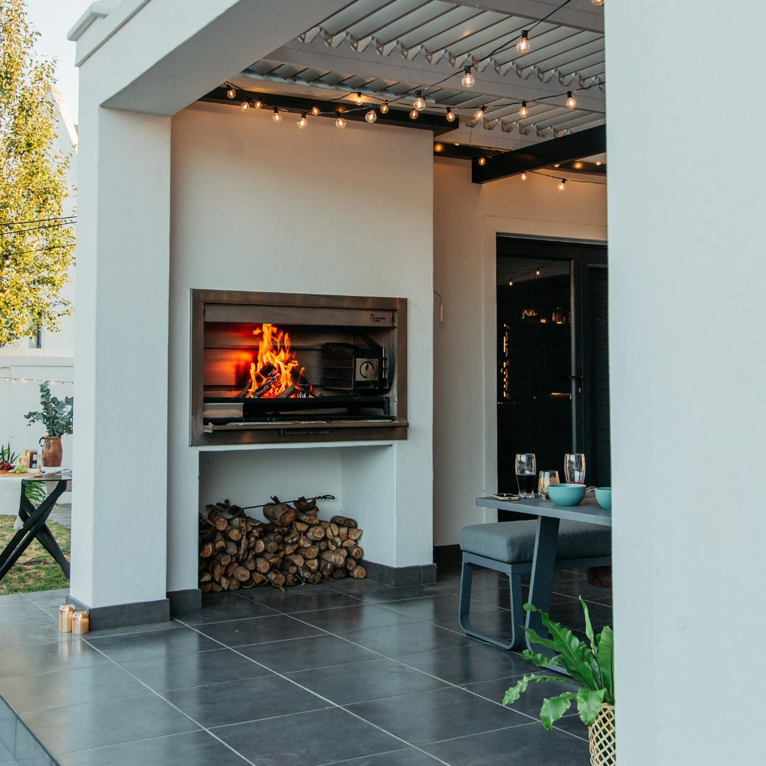 Classic String Lights Pro strung above an outdoor braai area with an open fire burning and a dining table set for the evening