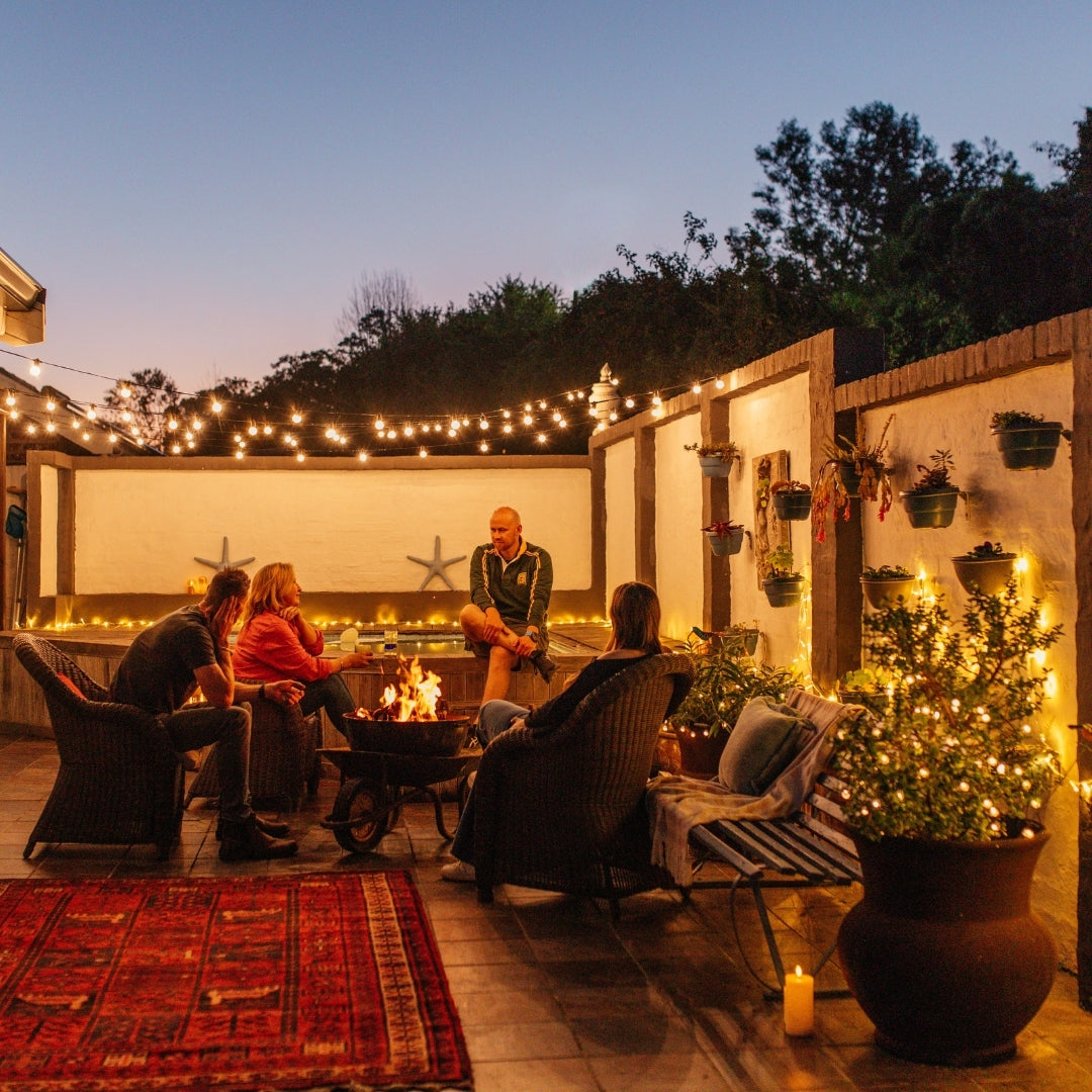 Classic String Lights Pro draped across an outdoor courtyard above a firepit and chairs and people at dusk