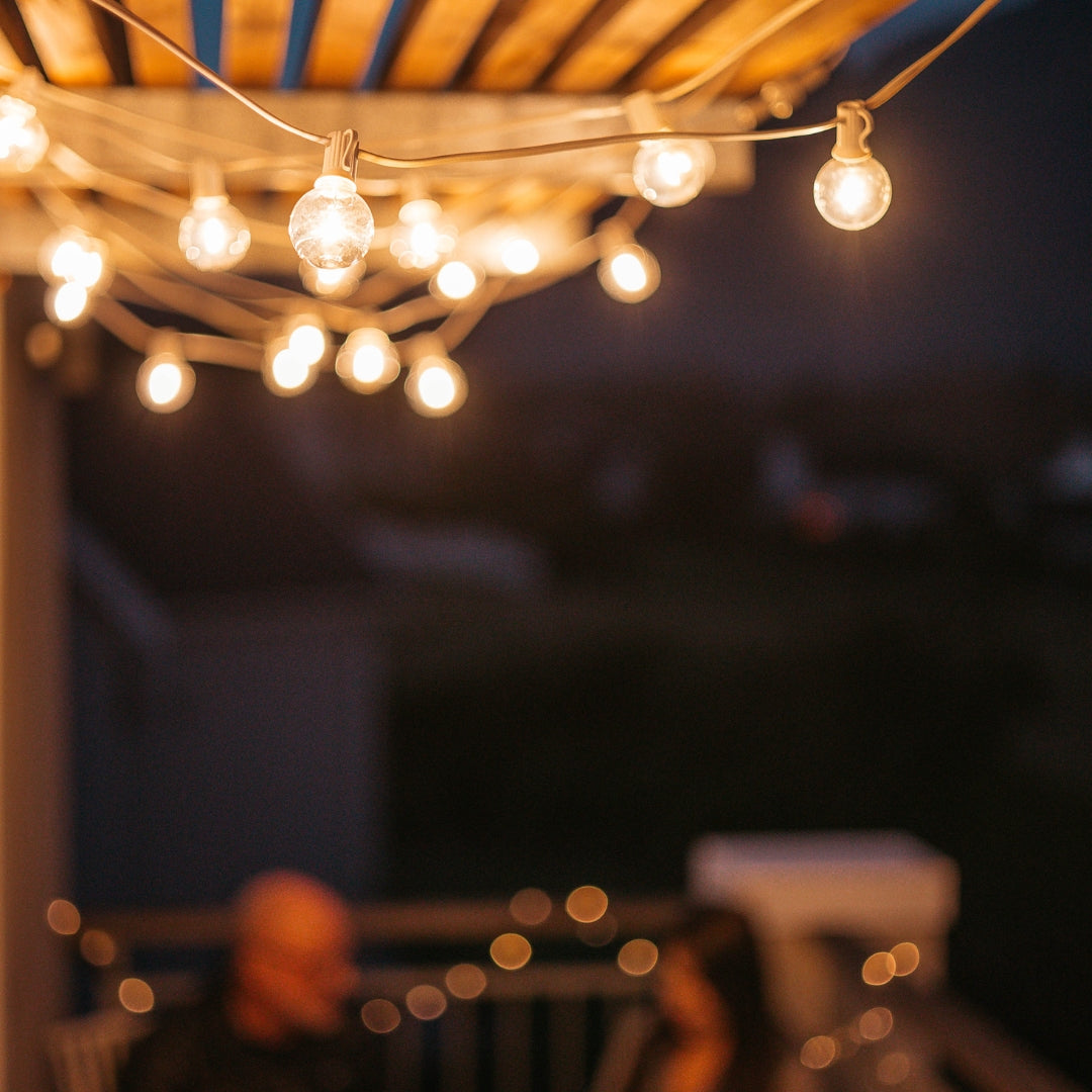 Classic string lights with G40 globe bulbs on white cable strung under a wooden pergola at night with warm ambient glow