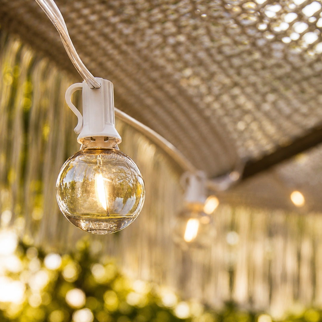 Close-up of G40 globe LED bulb on white cable hanging under a lattice pergola structure with warm white glow