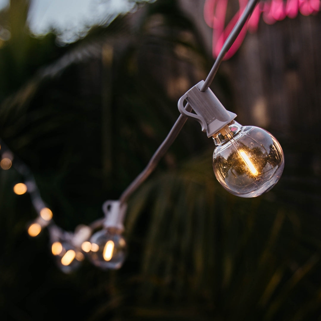 Close-up of G40 globe LED bulb on white cable glowing with warm white light at dusk with blurred background