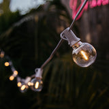 Close-up of G40 globe LED bulb on white cable glowing with warm white light at dusk with blurred background