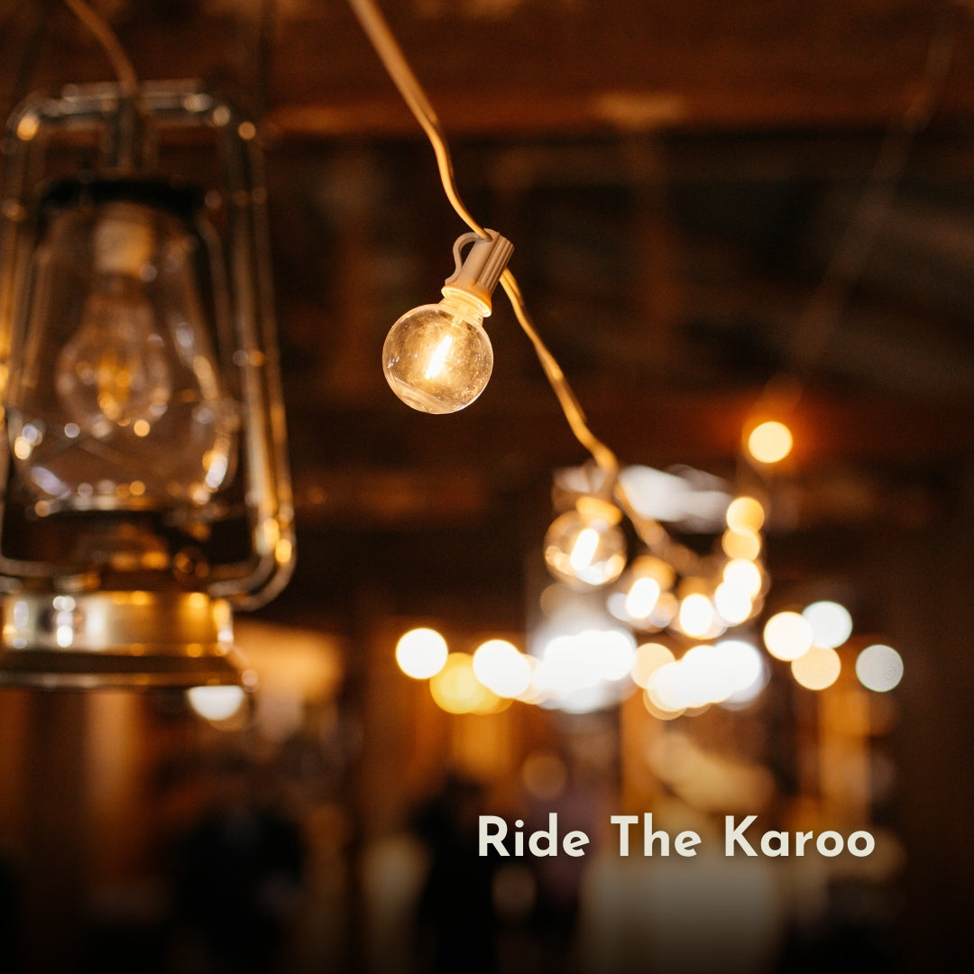 G40 globe bulb on white cable glowing alongside a vintage lantern at a Ride The Karoo indoor event with warm amber atmosphere