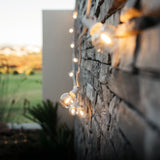 Classic string lights with G40 globe bulbs on white cable draped along an outdoor stone wall at dusk