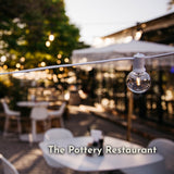 Classic string lights with G40 globe bulbs on white cable strung across The Pottery Restaurant outdoor terrace at sunset