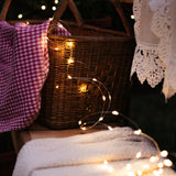 Wicker basket with copper fairy lights and checkered cloth on a wooden surface