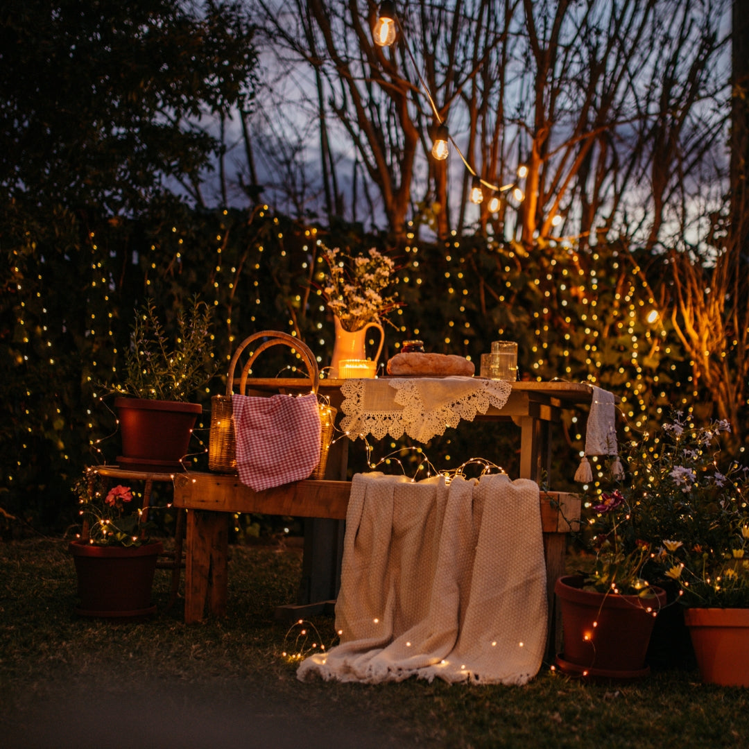 Outdoor setting with wooden table, chairs, and copper fairy lights in a garden.
