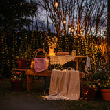 Outdoor setting with wooden table, chairs, and copper fairy lights in a garden.