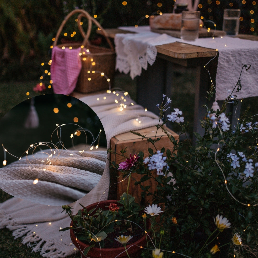 Outdoor setting with copper fairy lights, flowers, and a blanket on a table.