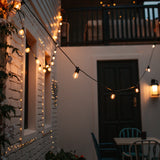 Fairy lights on a building exterior with a table and chairs in the foreground.