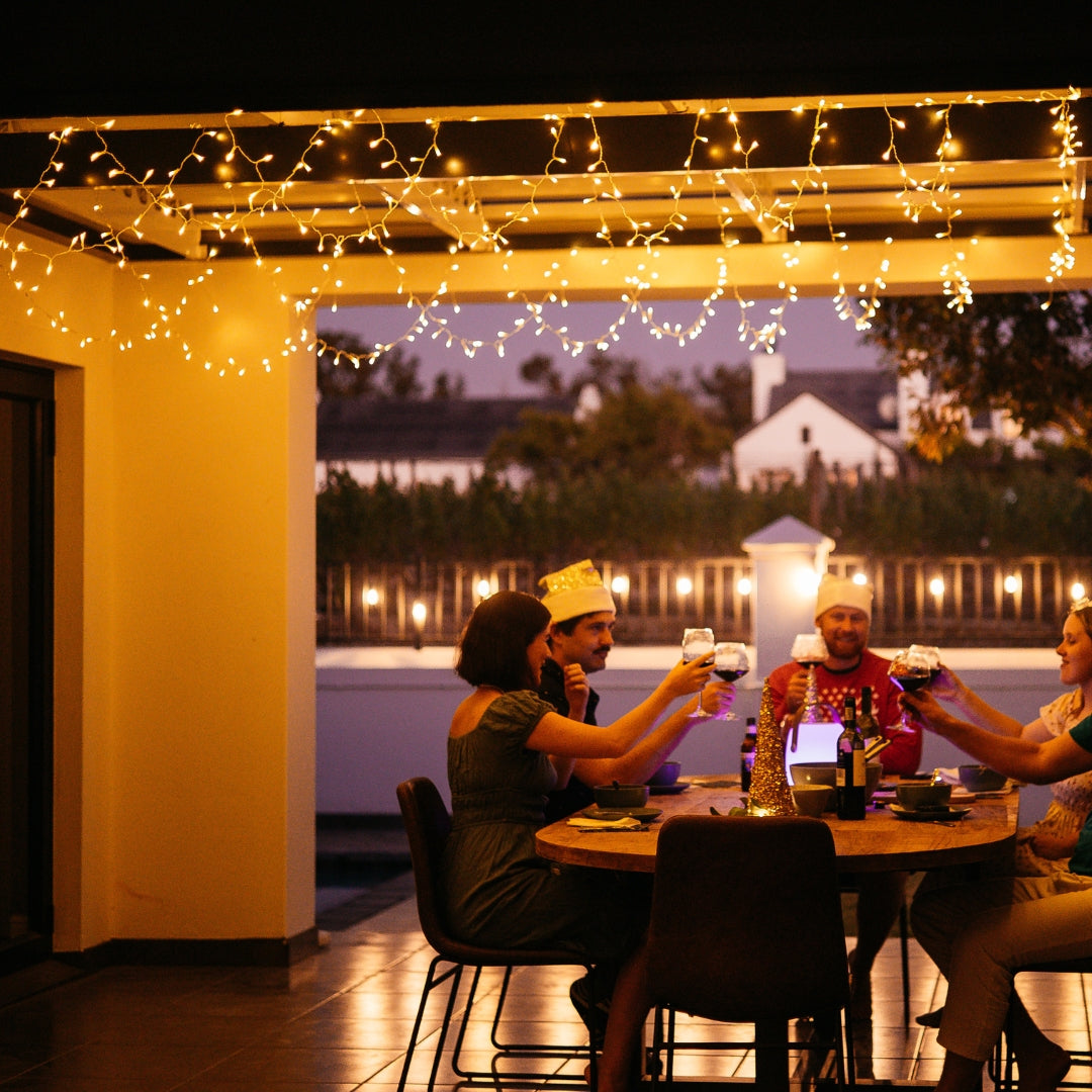 People enjoying a meal under curtain fairy lights on a patio at night.