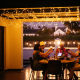 People enjoying a meal under curtain fairy lights on a patio at night.