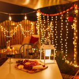 Dining table with charcuterie board and glasses, surrounded by curtain fairy lights and lanterns.