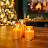 Three domed gold glass flameless LED candles grouped together on a wooden table with Christmas tree and fireplace bokeh background