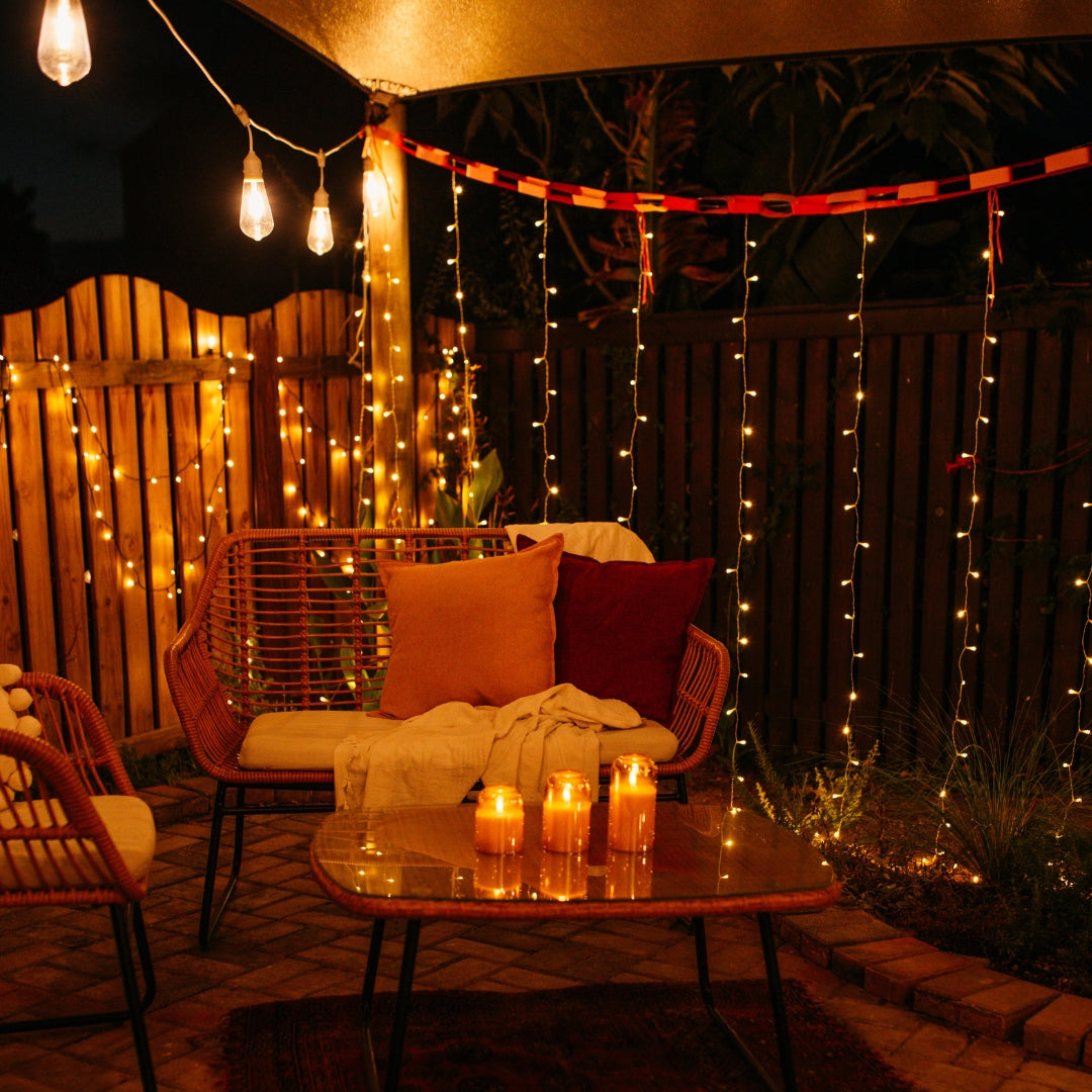 Domed glass flameless LED candles glowing on an outdoor coffee table surrounded by fairy lights and festoon lights on a cosy patio at night