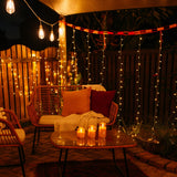 Domed glass flameless LED candles glowing on an outdoor coffee table surrounded by fairy lights and festoon lights on a cosy patio at night