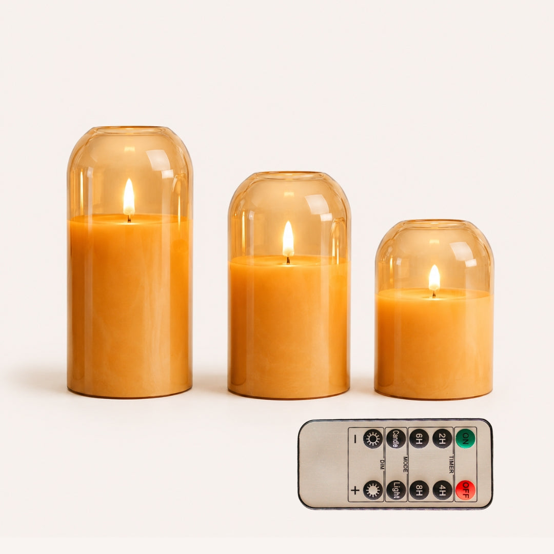 Set of three domed gold glass flameless LED candles in graduated heights with remote control on white background
