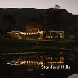 Evening scene at Stanford Hills with lit up structures and a pond reflecting lights with the mountains in th