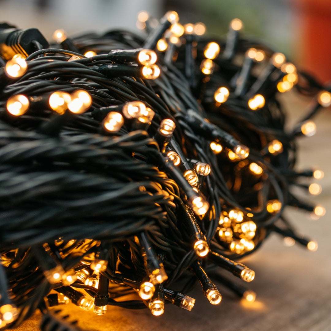 String of lights with warm glow on a blurred background. 300 warm white fairy lights draped through trees on dark green cable