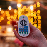 Hand holding RF remote control with festoon string lights glowing in the background