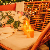 Flameless Candles in Glass scene with wicker furniture and floral cushion in a cozy setting.