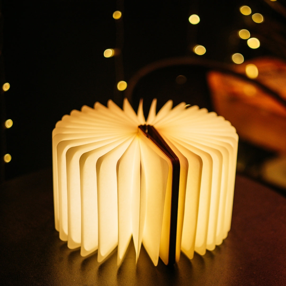 Foldable LED book light opened fully 360 degrees into a round lantern shape glowing with warm white light