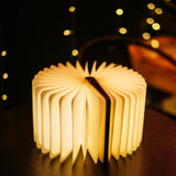 Foldable LED book light opened fully 360 degrees into a round lantern shape glowing with warm white light