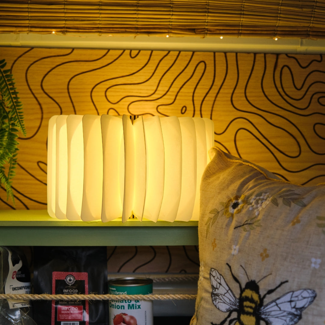 Foldable LED book light glowing on a shelf inside a camper van with warm white light