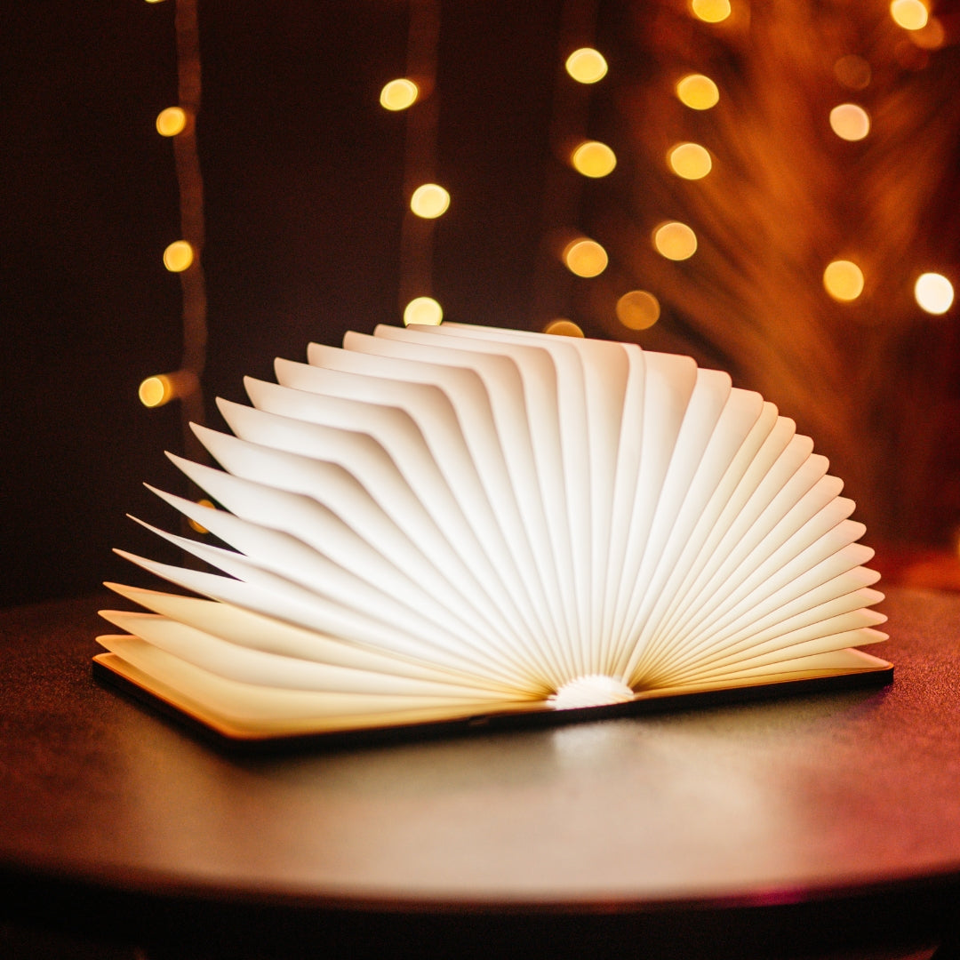 Foldable LED book light open and glowing with warm white light on a table with bokeh fairy lights in the background