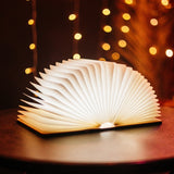 Foldable LED book light open and glowing with warm white light on a table with bokeh fairy lights in the background